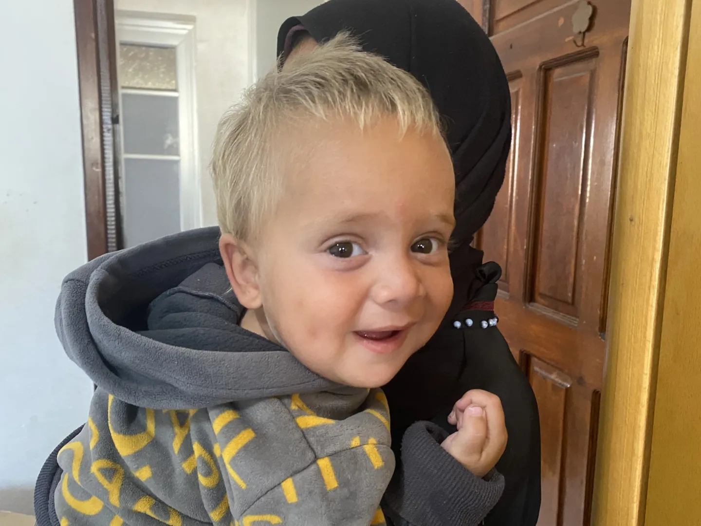 young boy smiling at the camera while being held by an adult