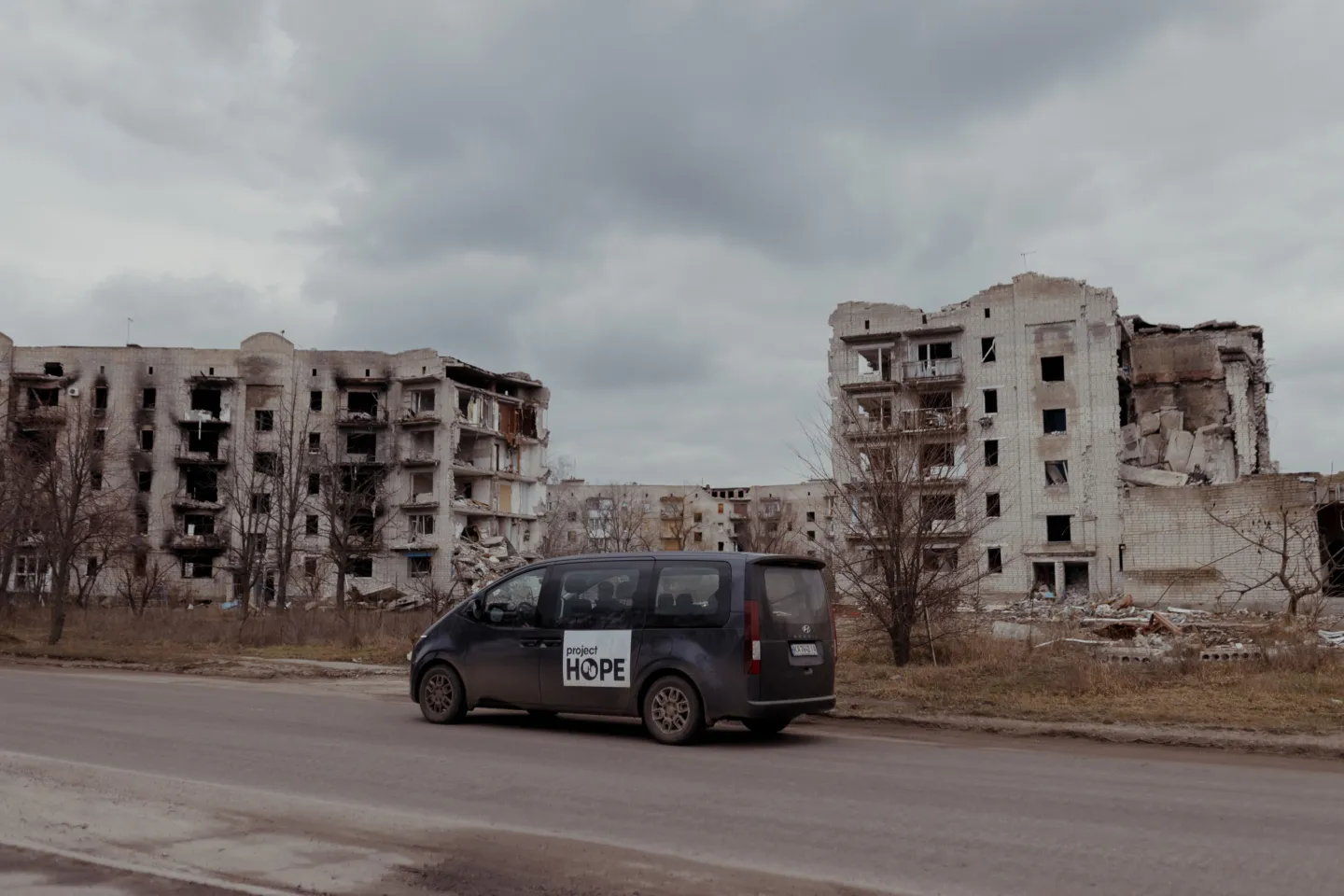 van with Project HOPE signage drives past destroyed buildings in Ukraine
