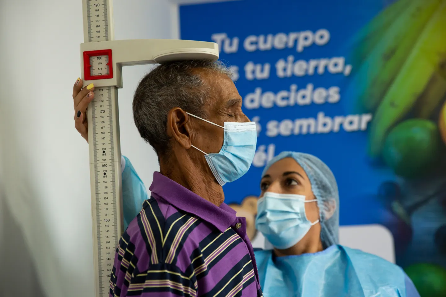 elderly man gets his height checked by medical staff in scrubs.