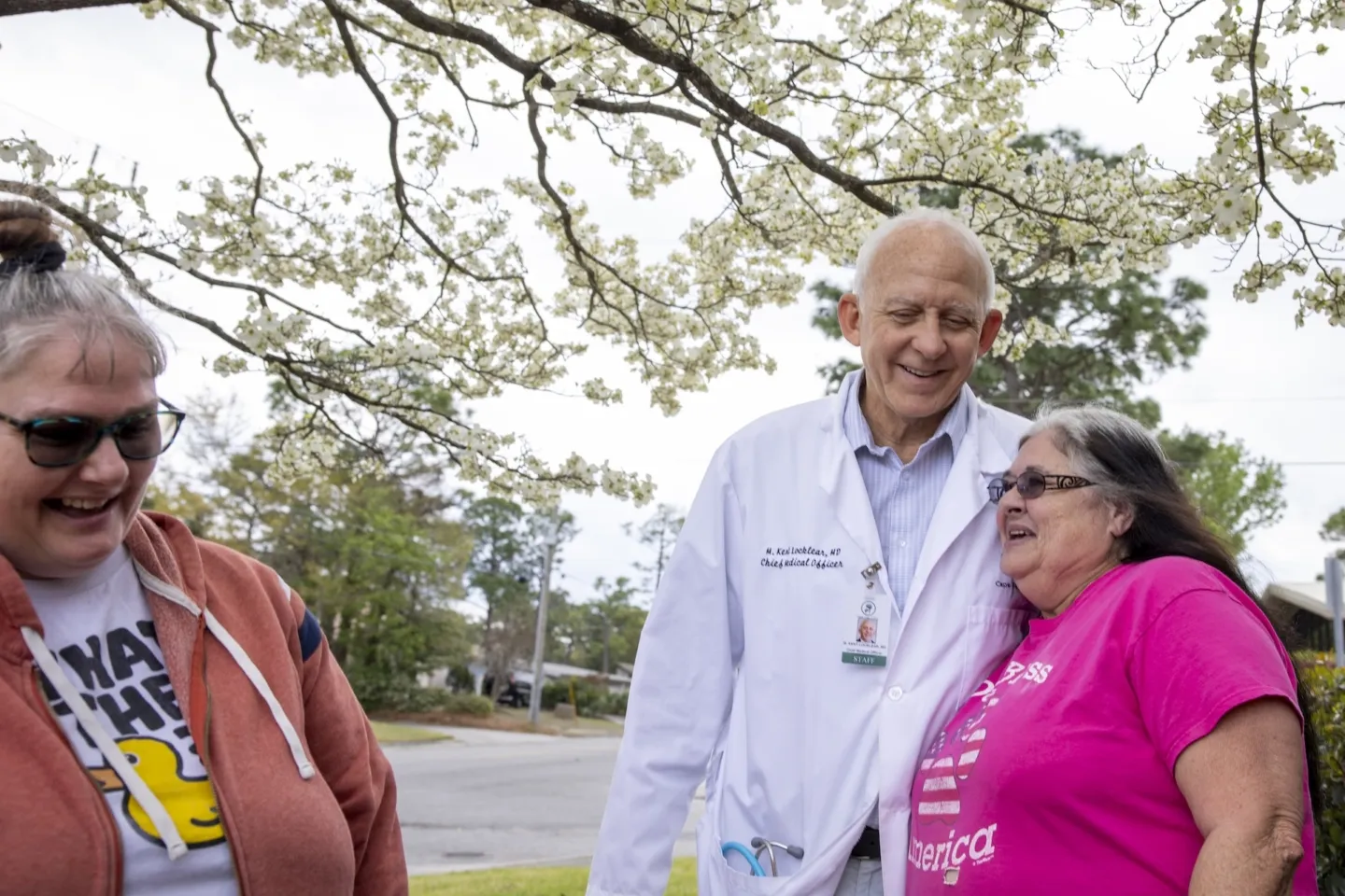 Three people standing together. A doctor hugs a woman