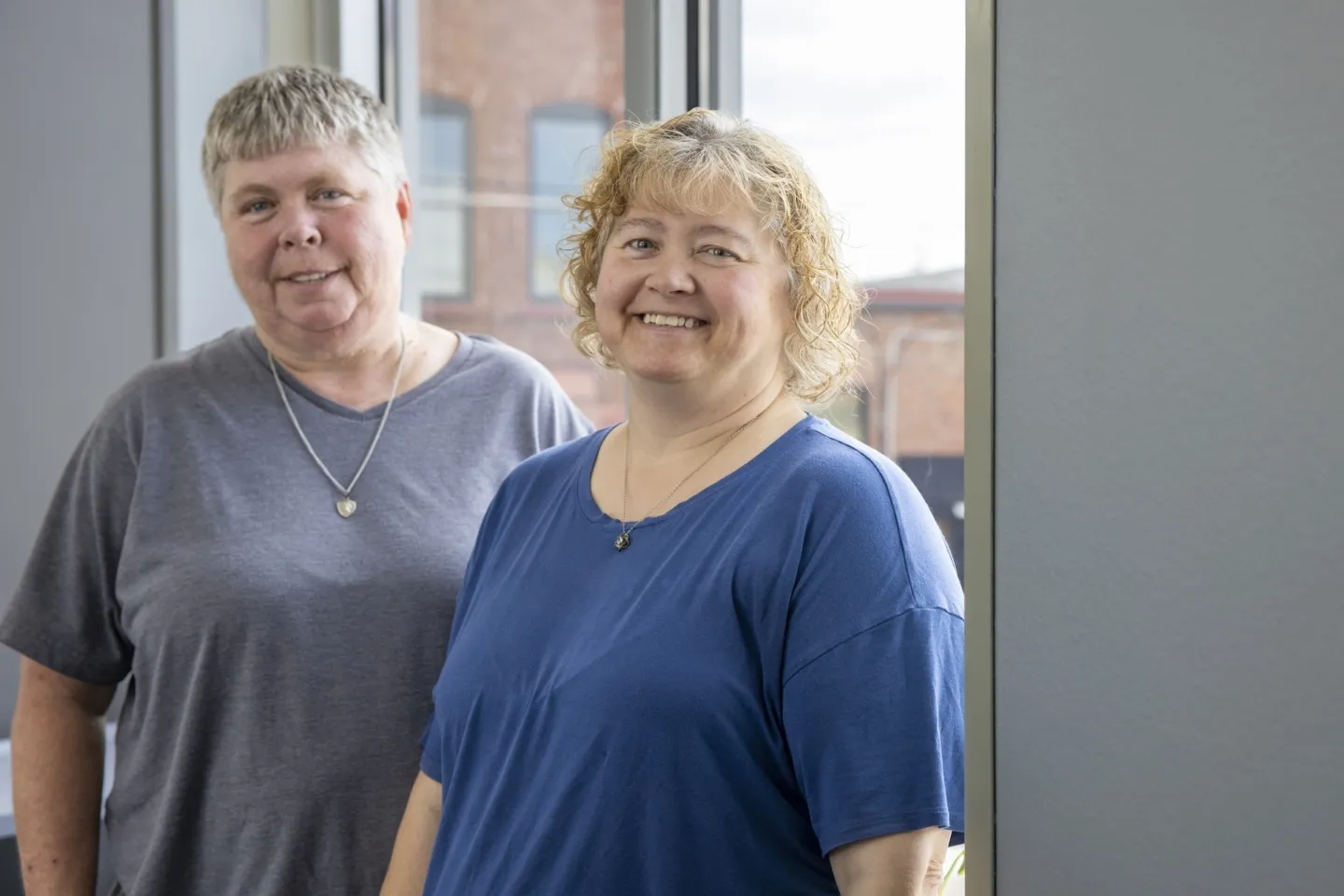 Two women in blue shirts smiling to camera
