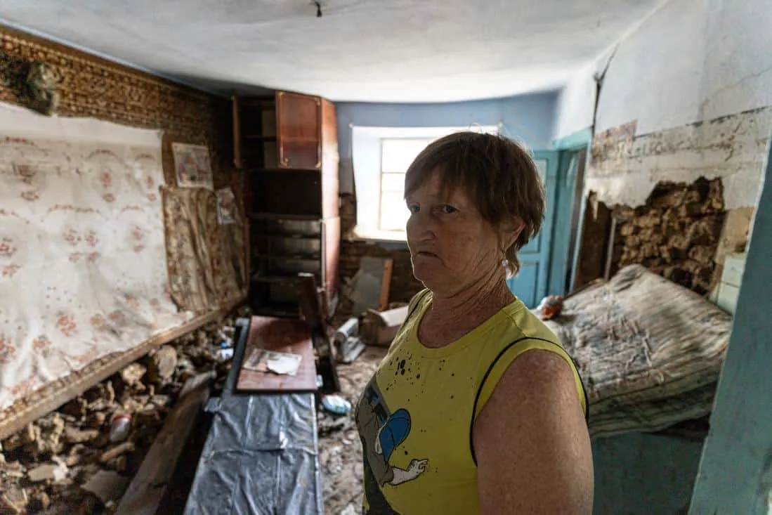 Woman in yellow shirt standing in a destroyed home due to flooding in Ukraine