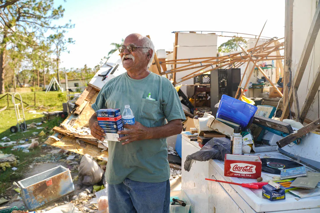 older man stands in front of destroyed home from hurricane