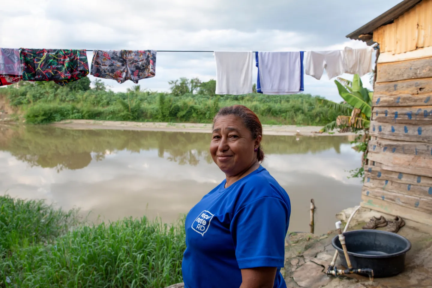 Dominican woman standing in front of home next to river