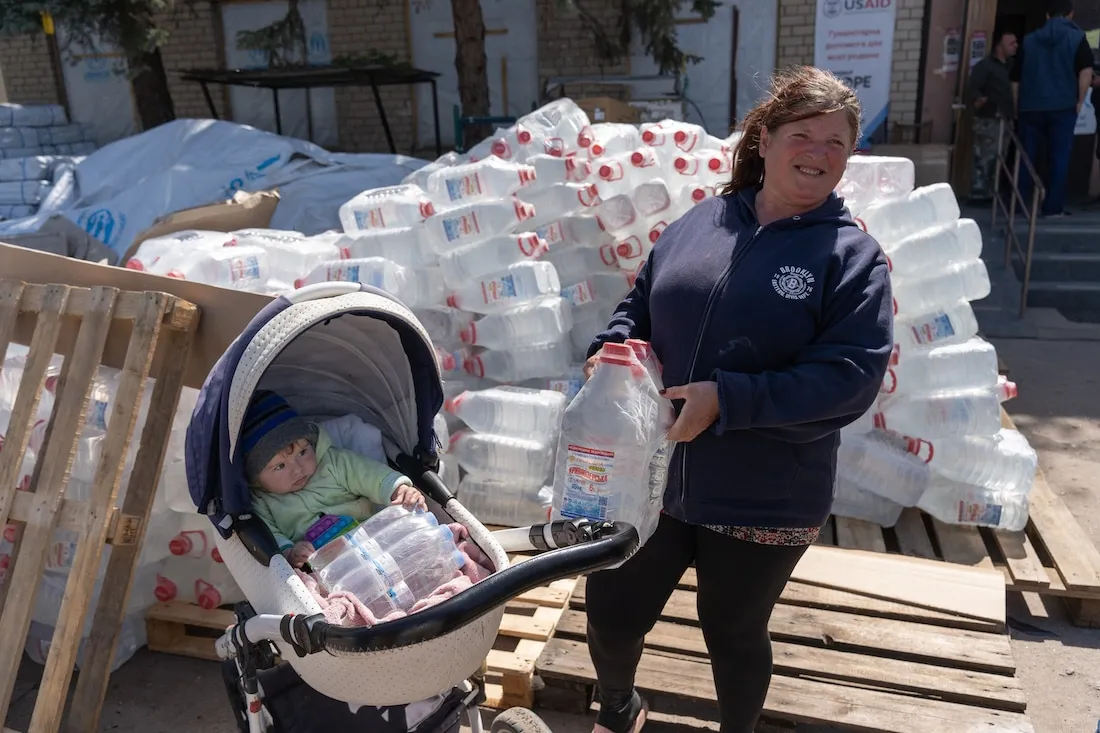 woman with child in stroller surrounded by water jugs