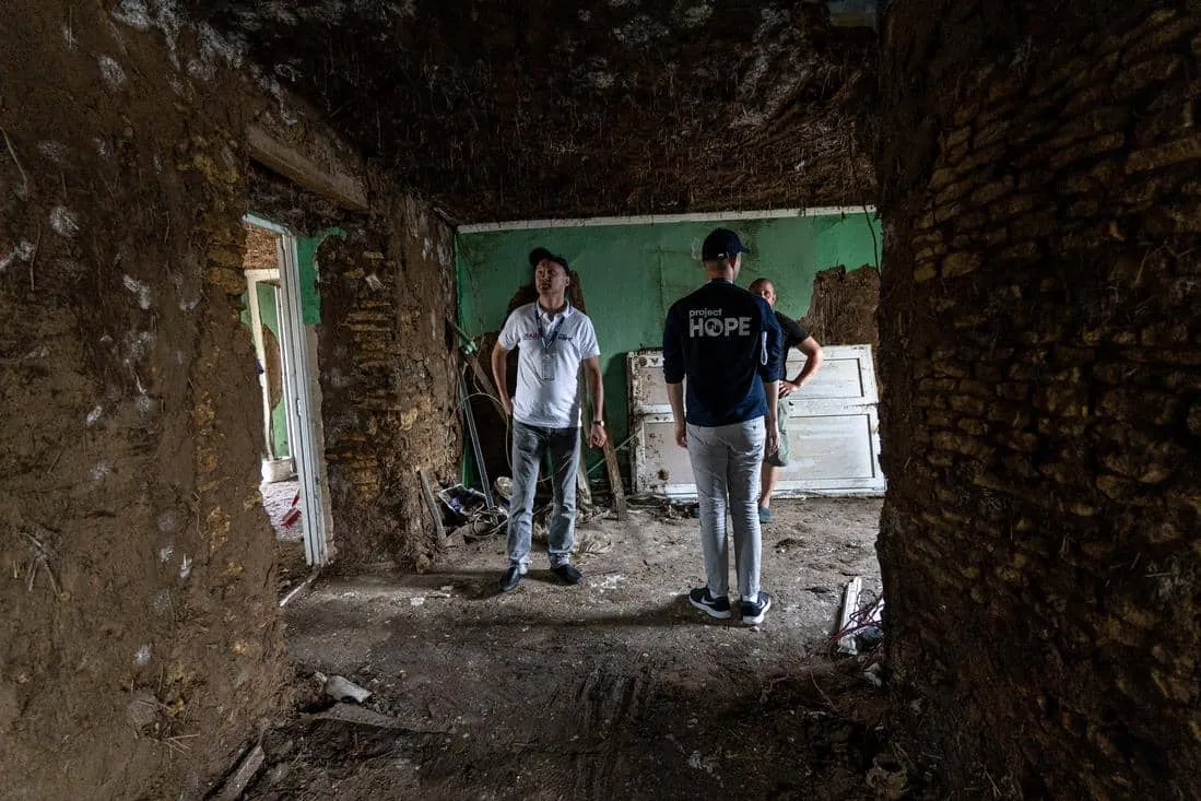 Three people standing in destroyed home in Ukraine