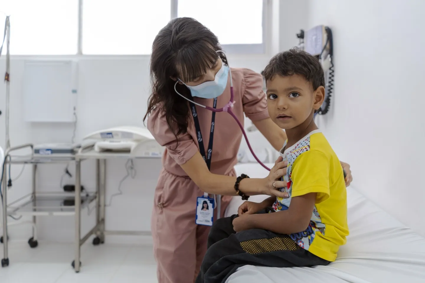 young boy looking at camera, gets his lungs checked by nurse