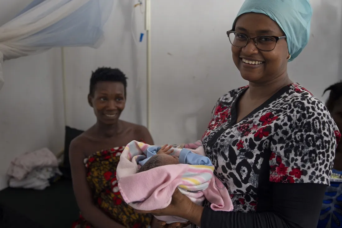 Midwife holds newborn while mother looks on