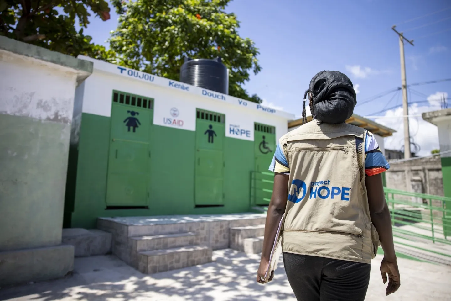 woman in Project HOPE vest walking by washrooms in Haiti