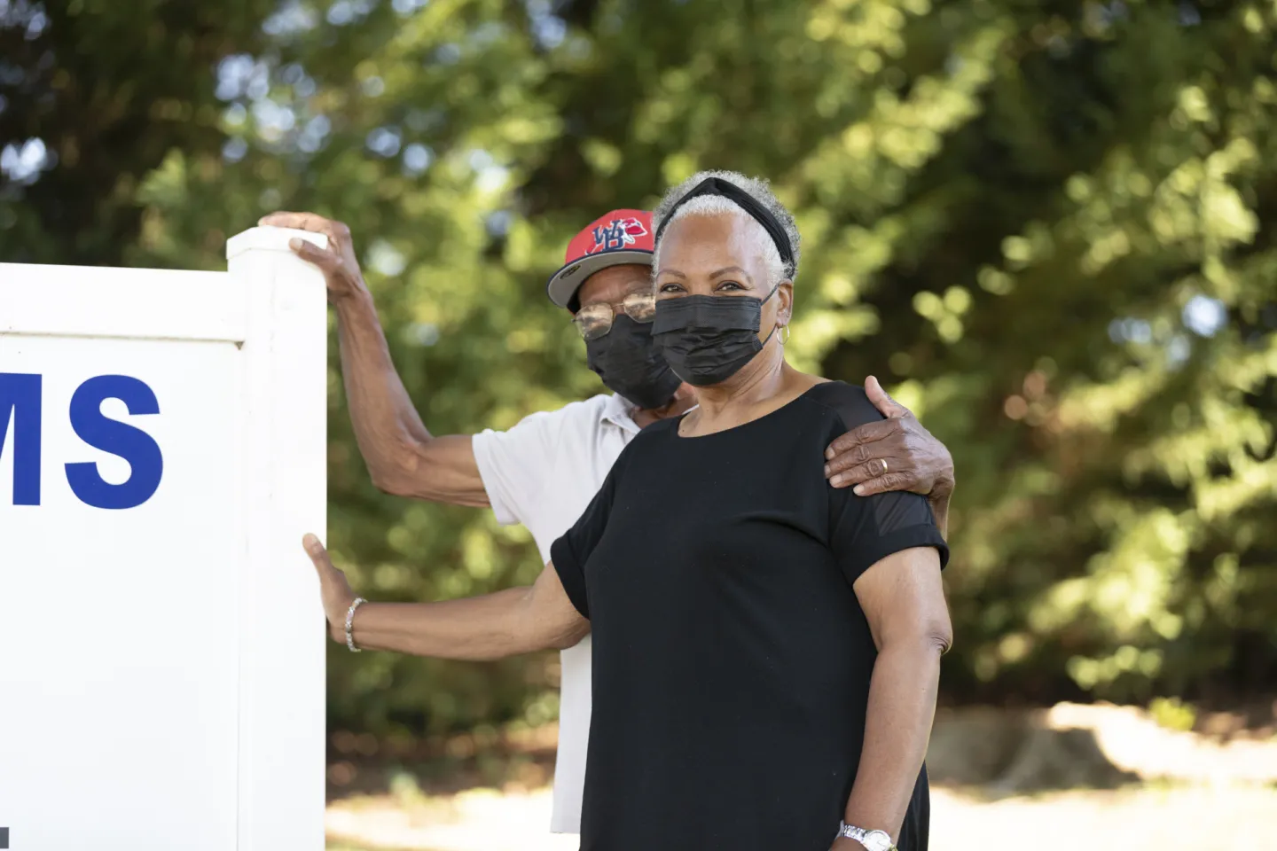 An elderly couple in face masks stand in front of a medical sign