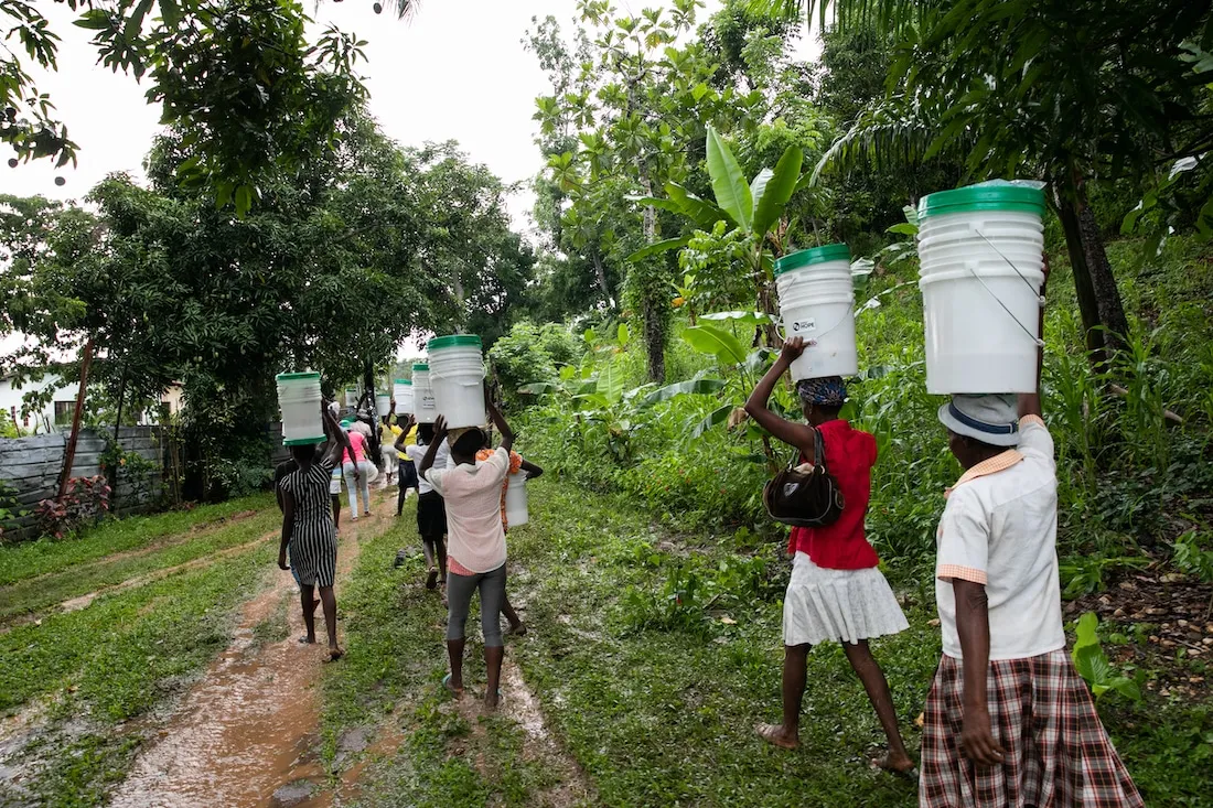 a line of people walking away with hygiene kits on their heads.