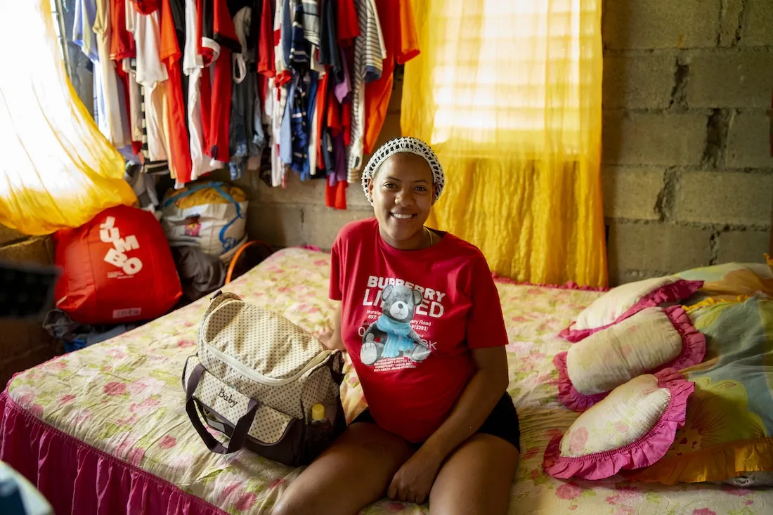 pregnant woman sitting on bed smiling to camera.