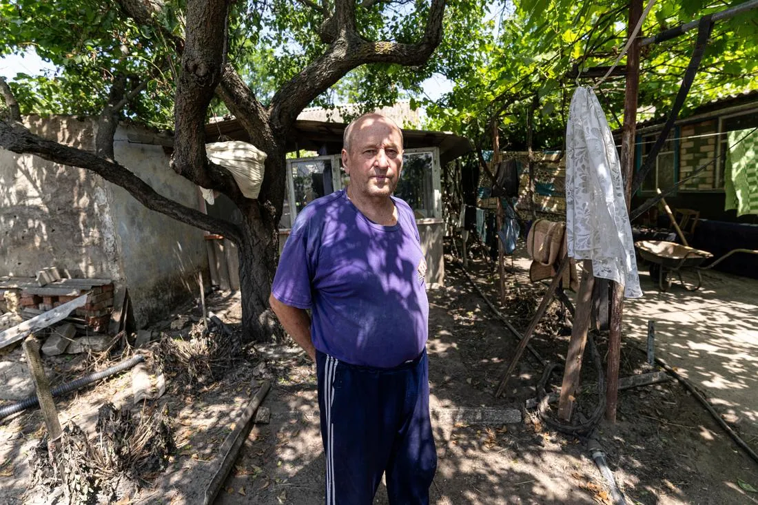 man in purple shirt standing in front of home