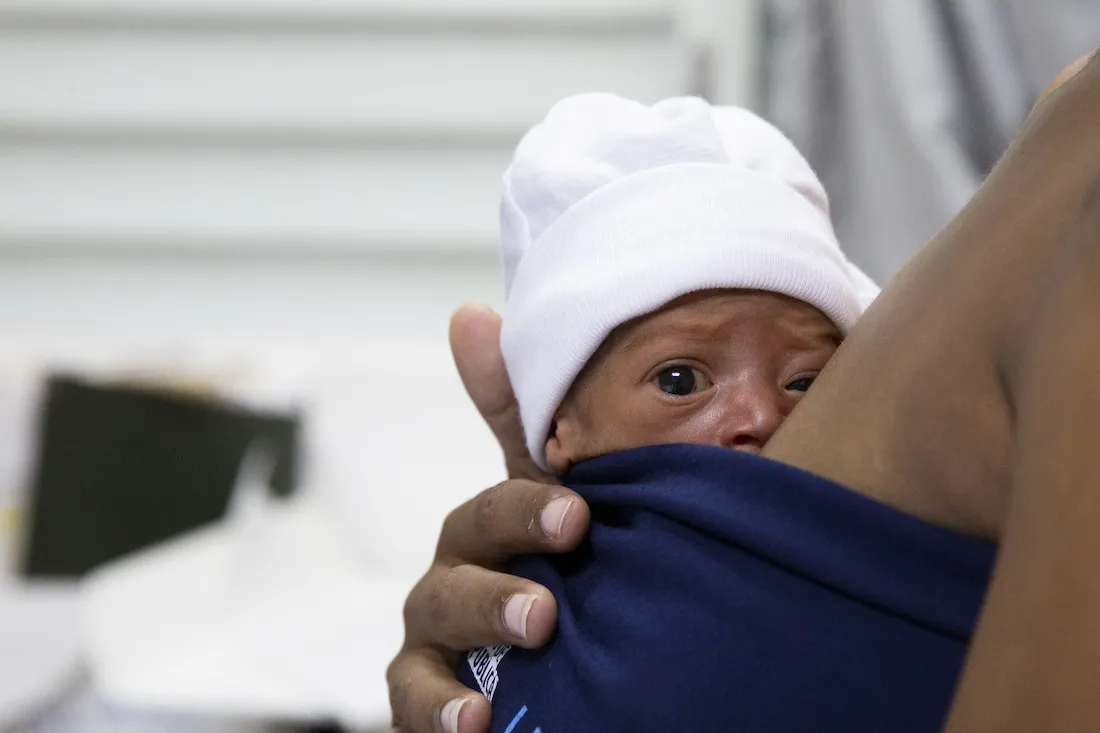 Newborn baby strapped to breast of mother