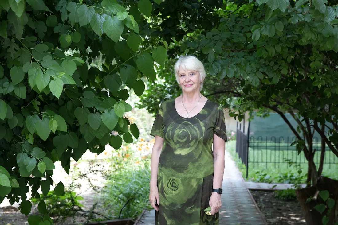 elderly woman in green dress standing among green trees