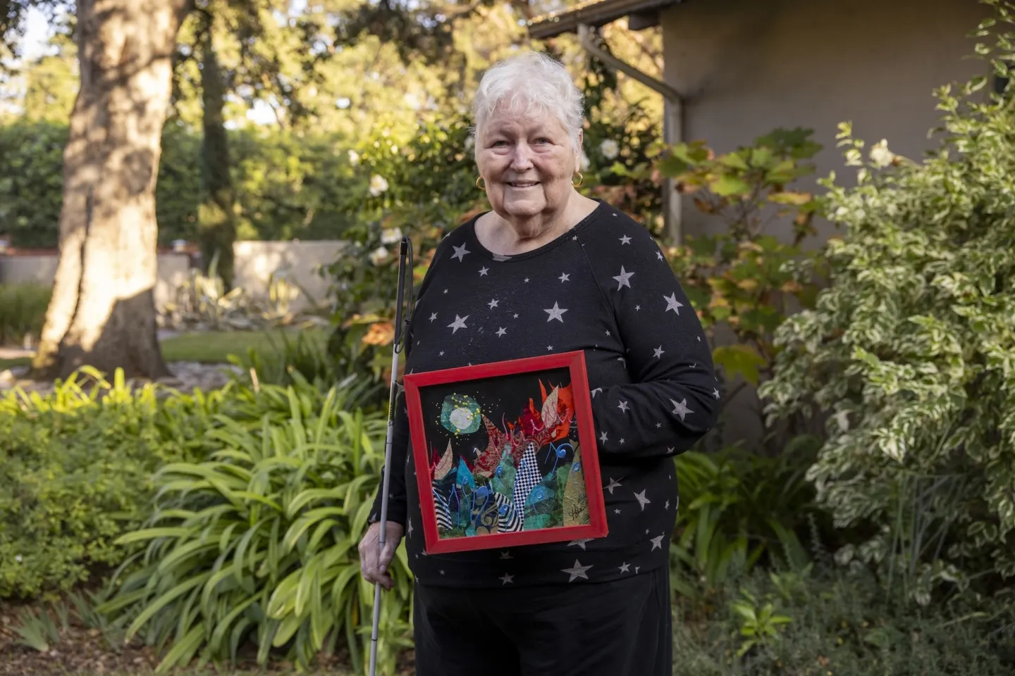 elderly woman holds up artwork