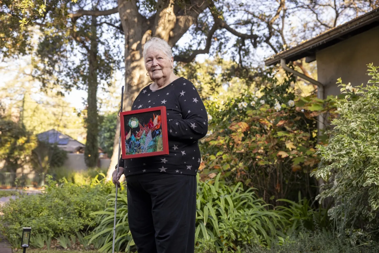 older woman stands outside holding artwork