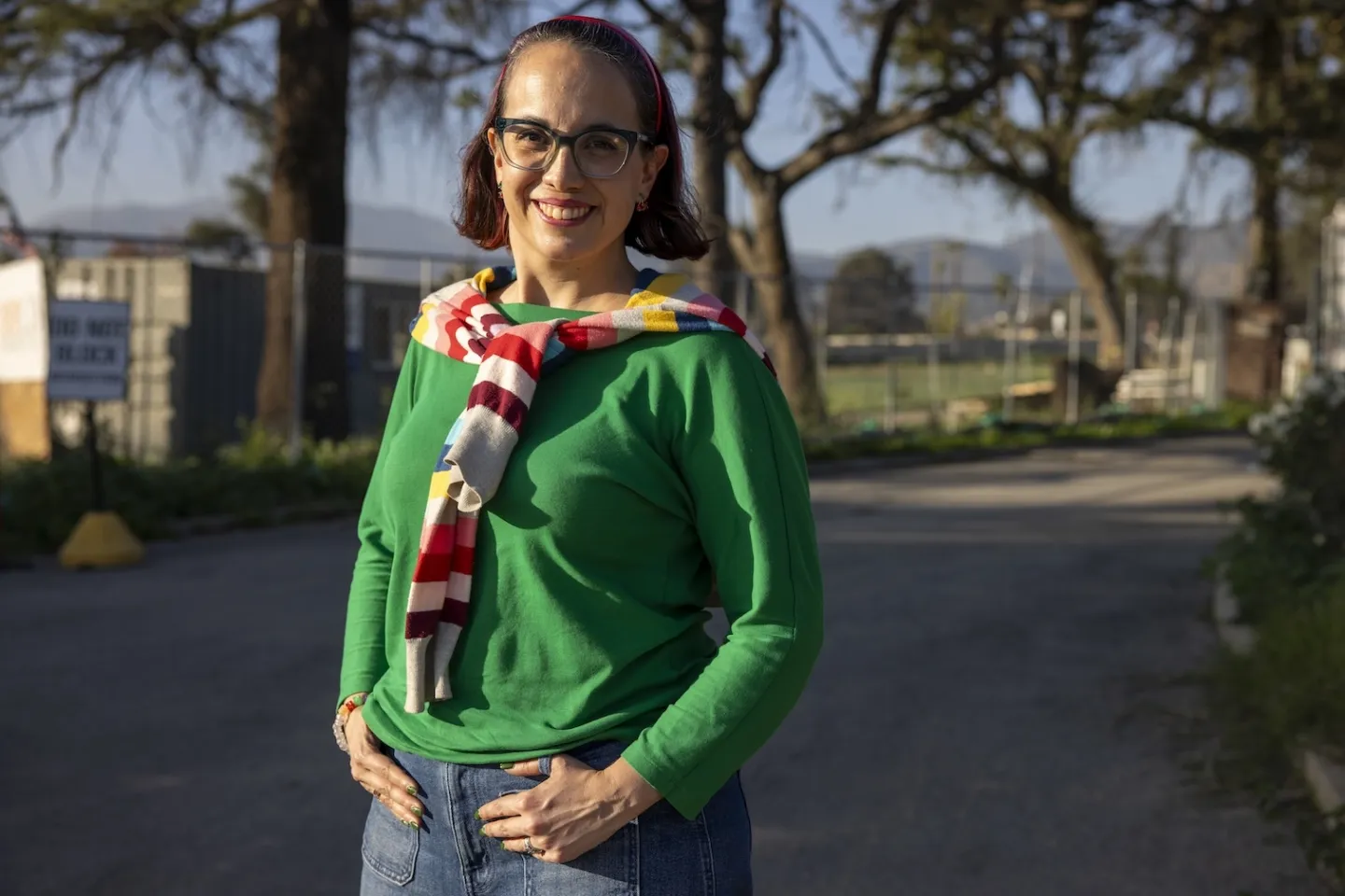 woman in glasses and green sweater with striped scarf, poses for the camera