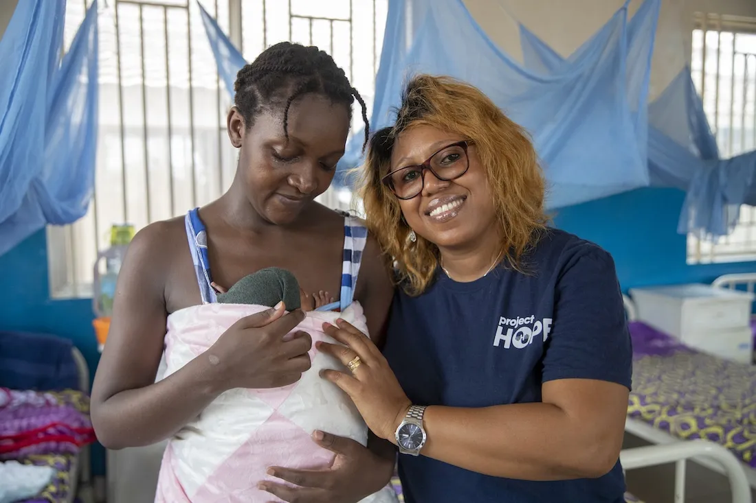 Two women standing next to each other and smiling. One is holding their newborn baby