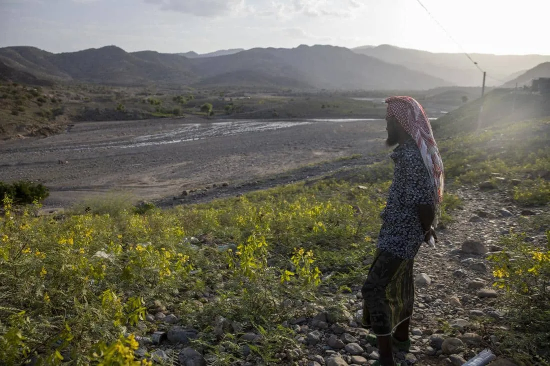 wide angle shot of man facing away from camera, looping out onto drought-ridden landscape