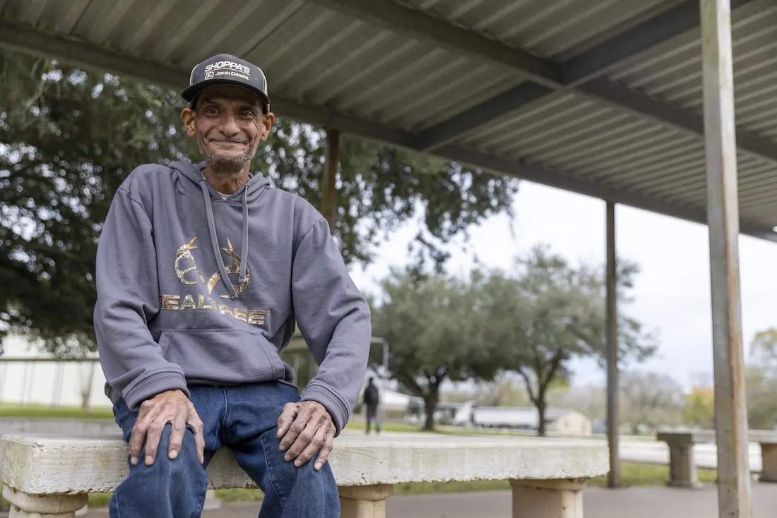 older man sits on a park bench and smiles