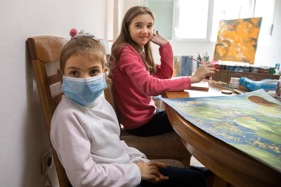Two girls sit at a table doing art.