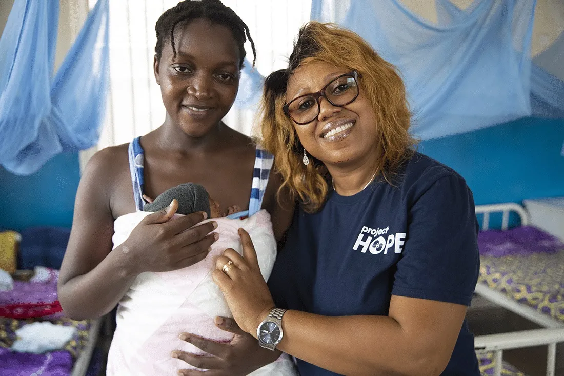 Two women standing together. One woman is holding a newborn baby