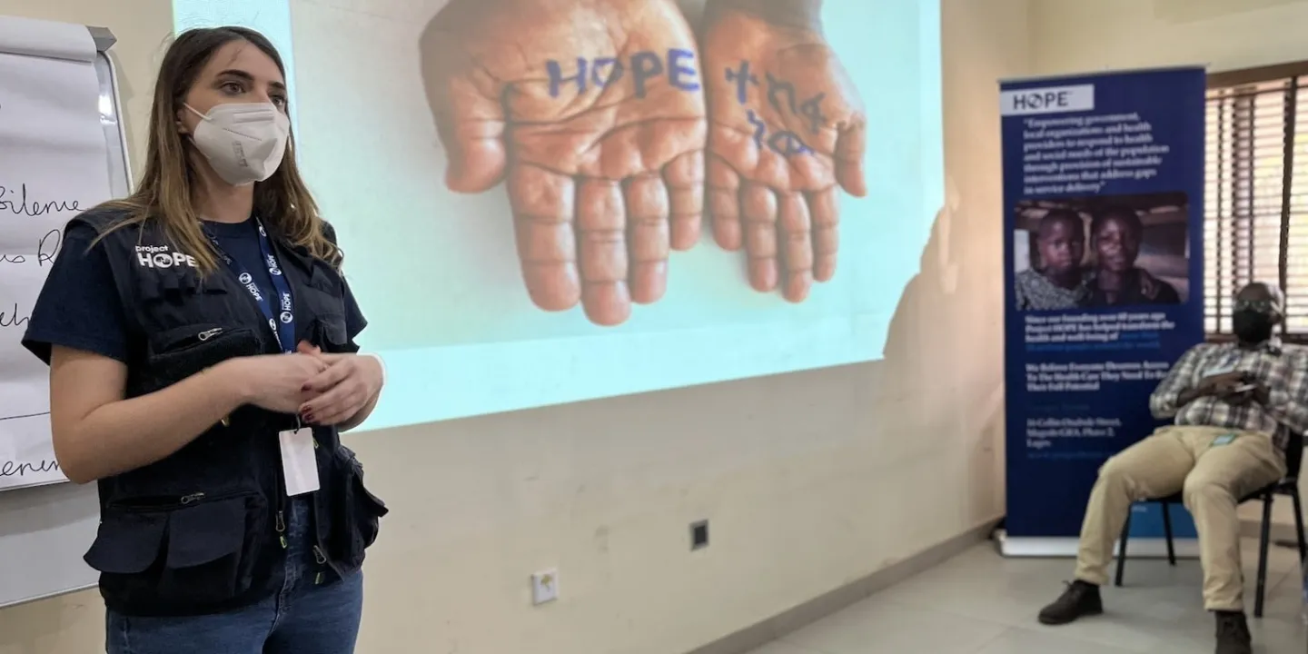 Project HOPE staff, in facemask, speaks about mental health to audience