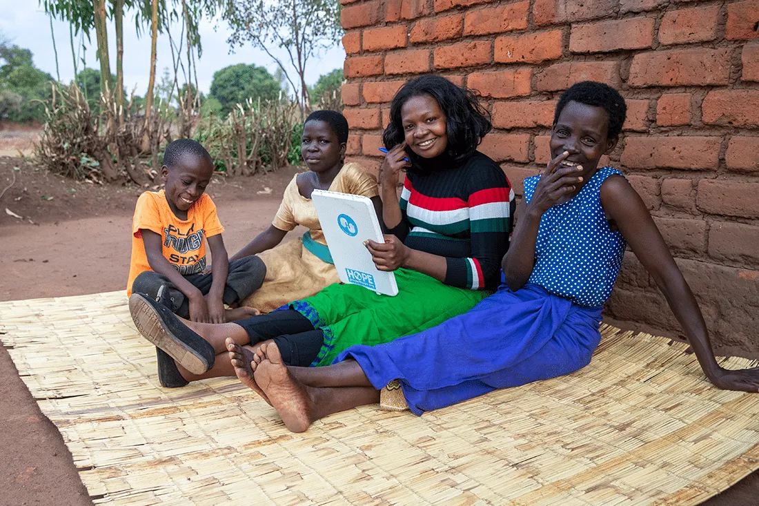 group of people sitting on straw rug outside of house