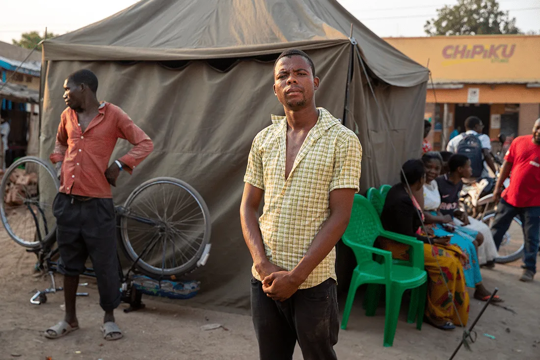 man in a yellow shirt stands in front of a medical tent