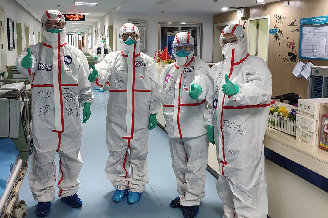 Doctors wearing protective gear give thumps up sign.